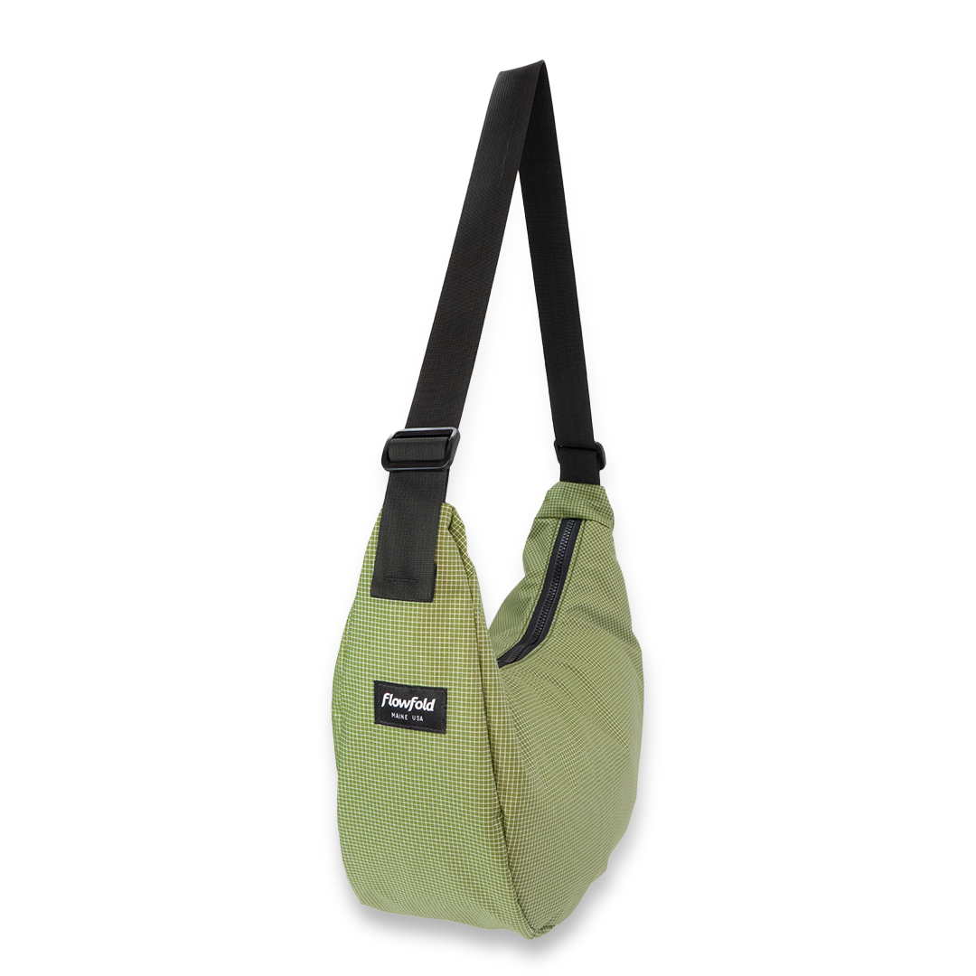 Green crescent bag with a black strap on a white background