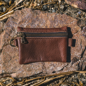 Brown leather pouch with a zipper on a rocky surface