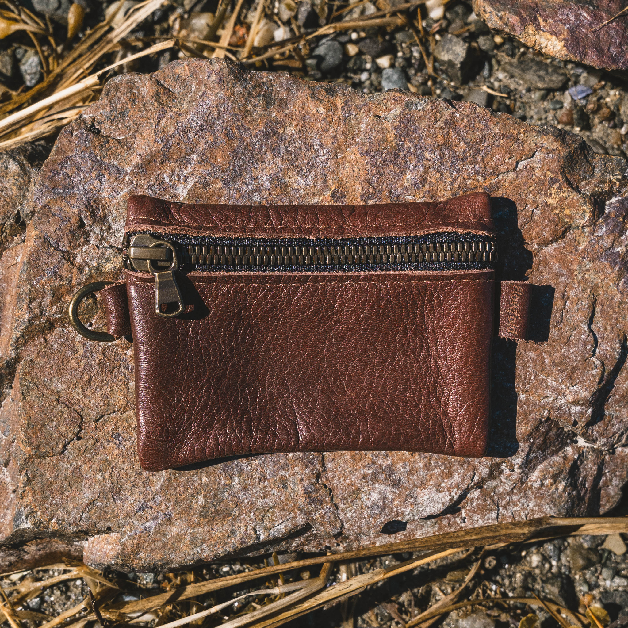 Brown leather pouch with a zipper on a rocky surface