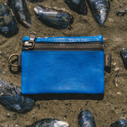 Blue leather pouch with a zipper on a sandy surface with shells.