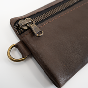 Close-up of a brown leather pouch with a zipper and gold ring on a white background