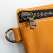 Close-up of a yellow leather pouch with a zipper and gold ring on a white background