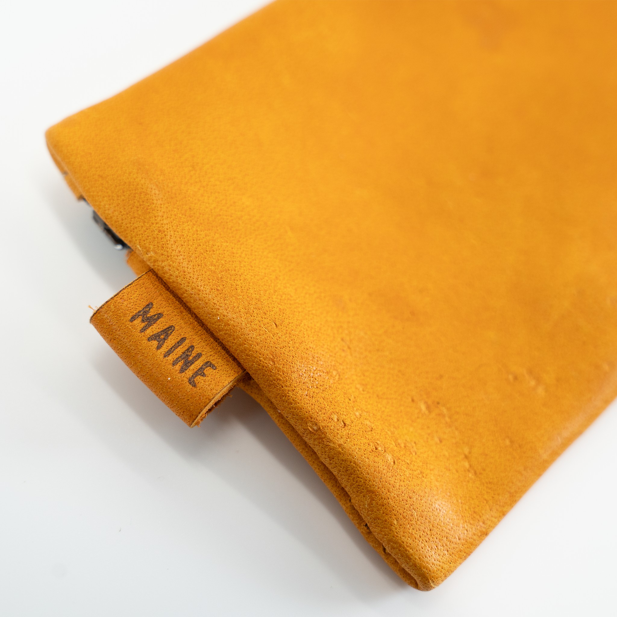Close-up of a mustard yellow leather with 'MAINE' label on a white background