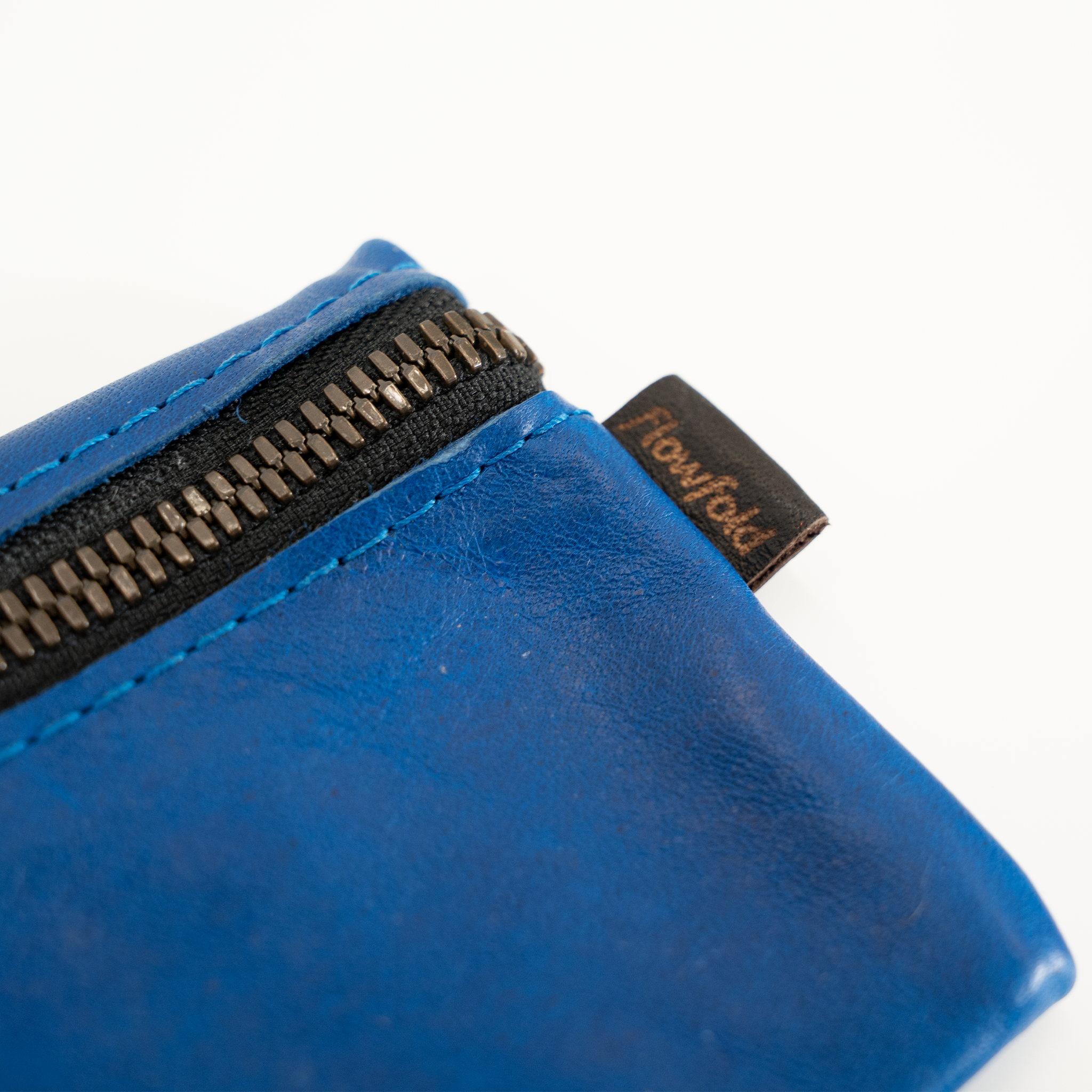 Blue leather pouch with zipper and brand tag on a white background
