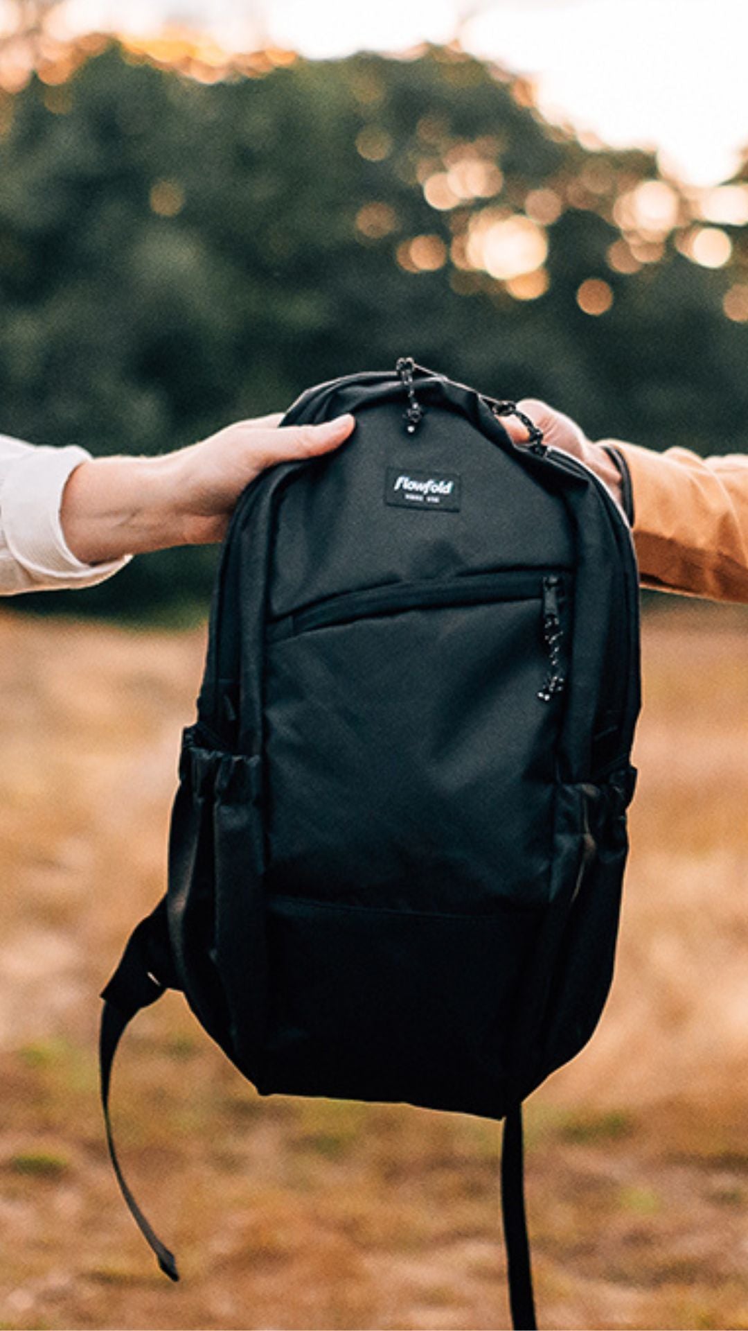Two people holding a black flowfold backpack between them