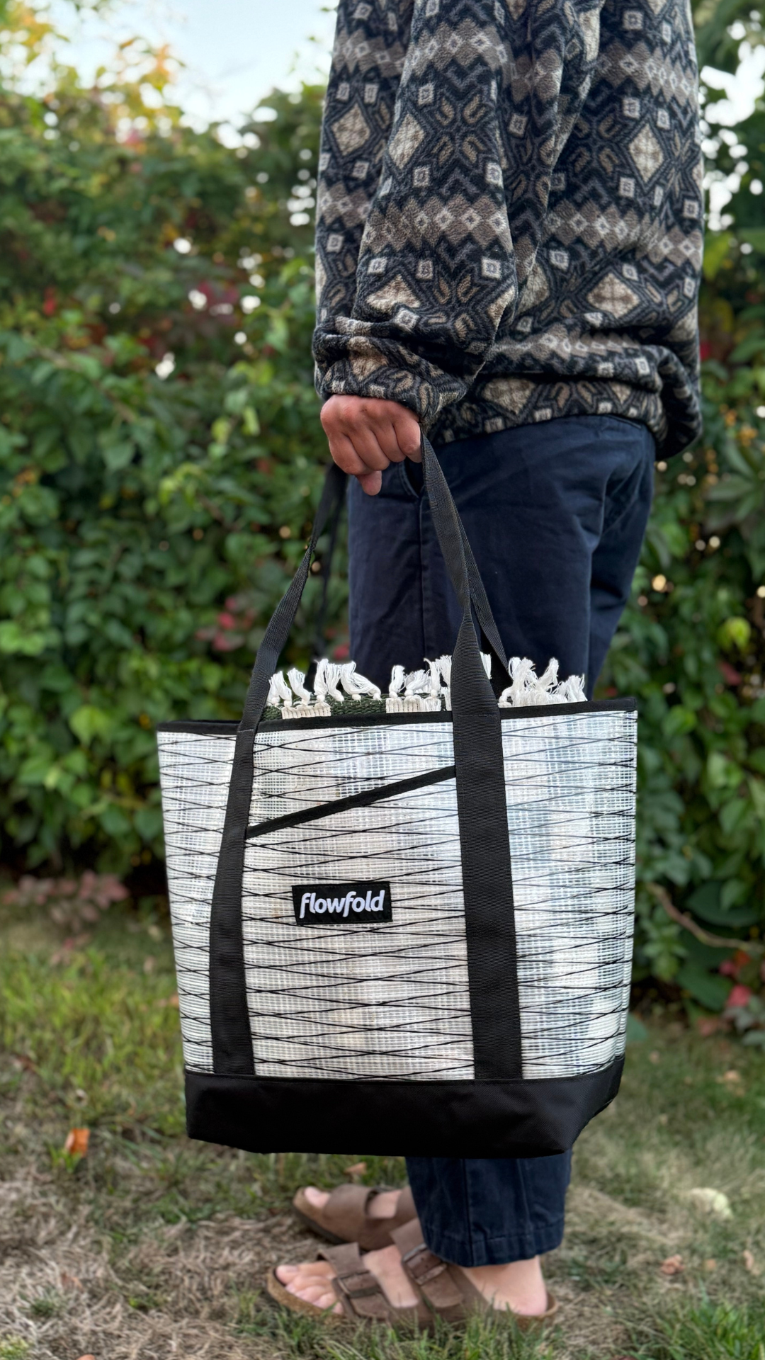 Person holding a recycled sailcloth tote bag outdoors with greenery in the background