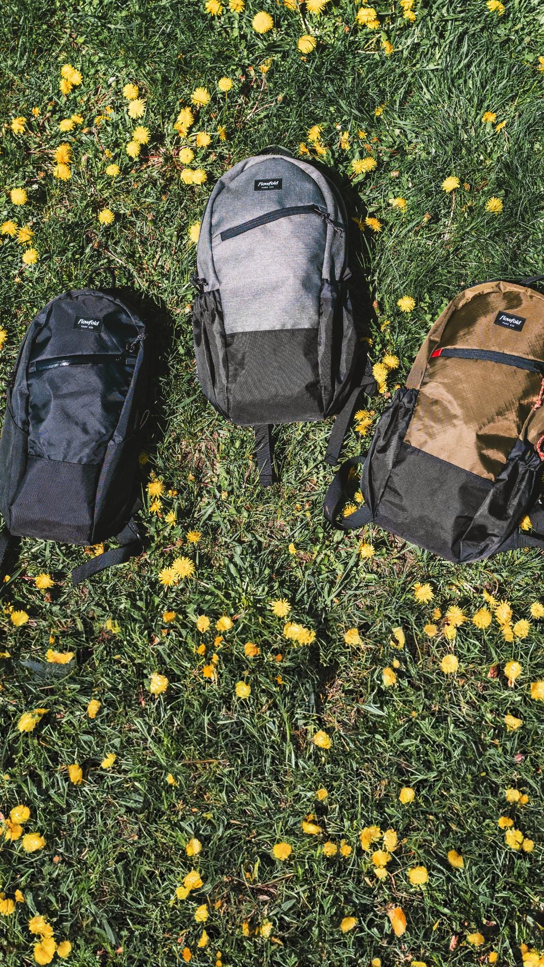 3 backpacks in different sizes laying on the ground in a field of dandelions.
