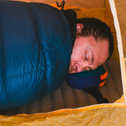 Man sleeping in a blue sleeping bag inside a yellow tent using the sambob x flowfold blue and purple fleece grid belt bag as a pillow when hiking