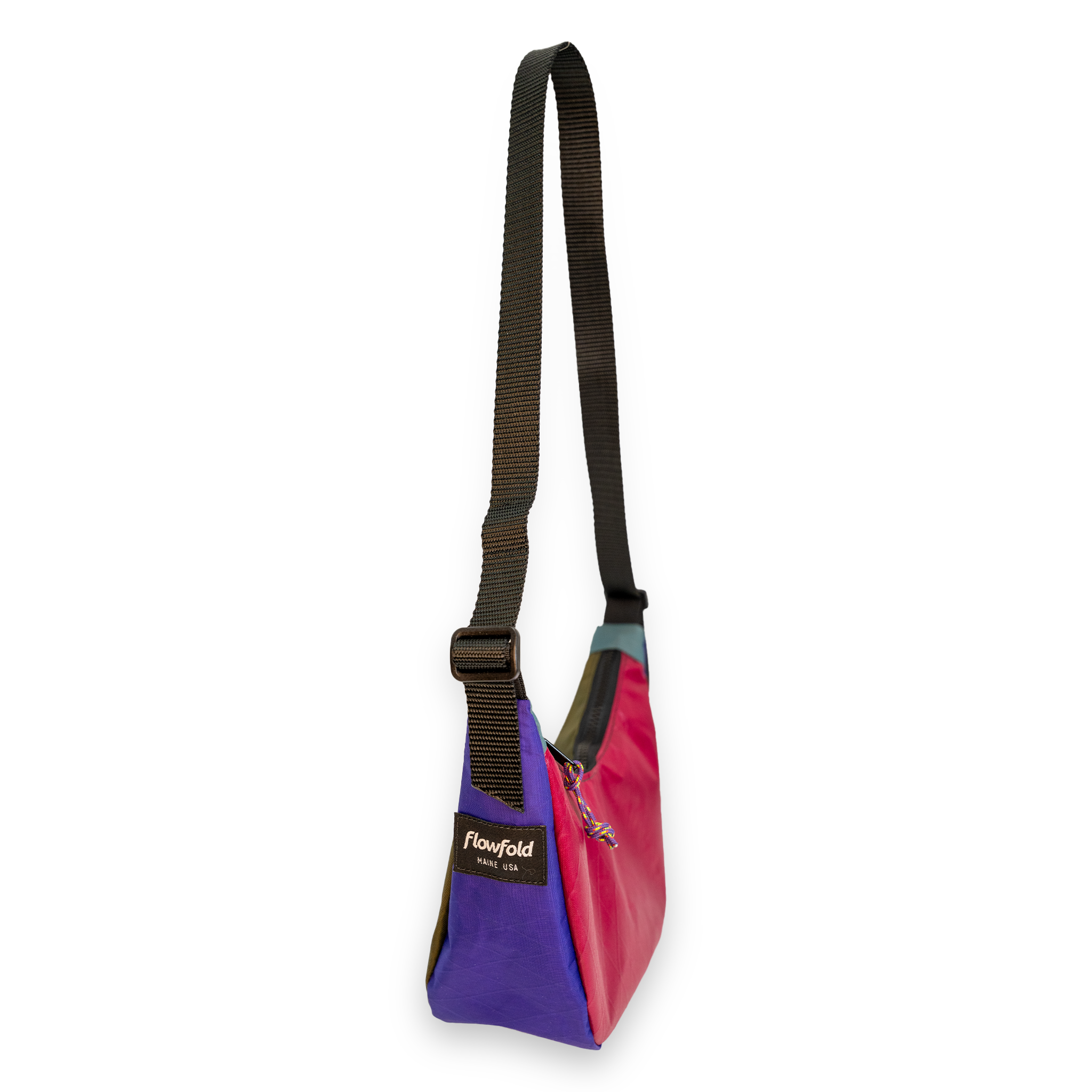 A multicolor crossbody bag by Flowfold, featuring a purple front pocket, a pink side panel, a teal top trim, and a black adjustable webbing strap.