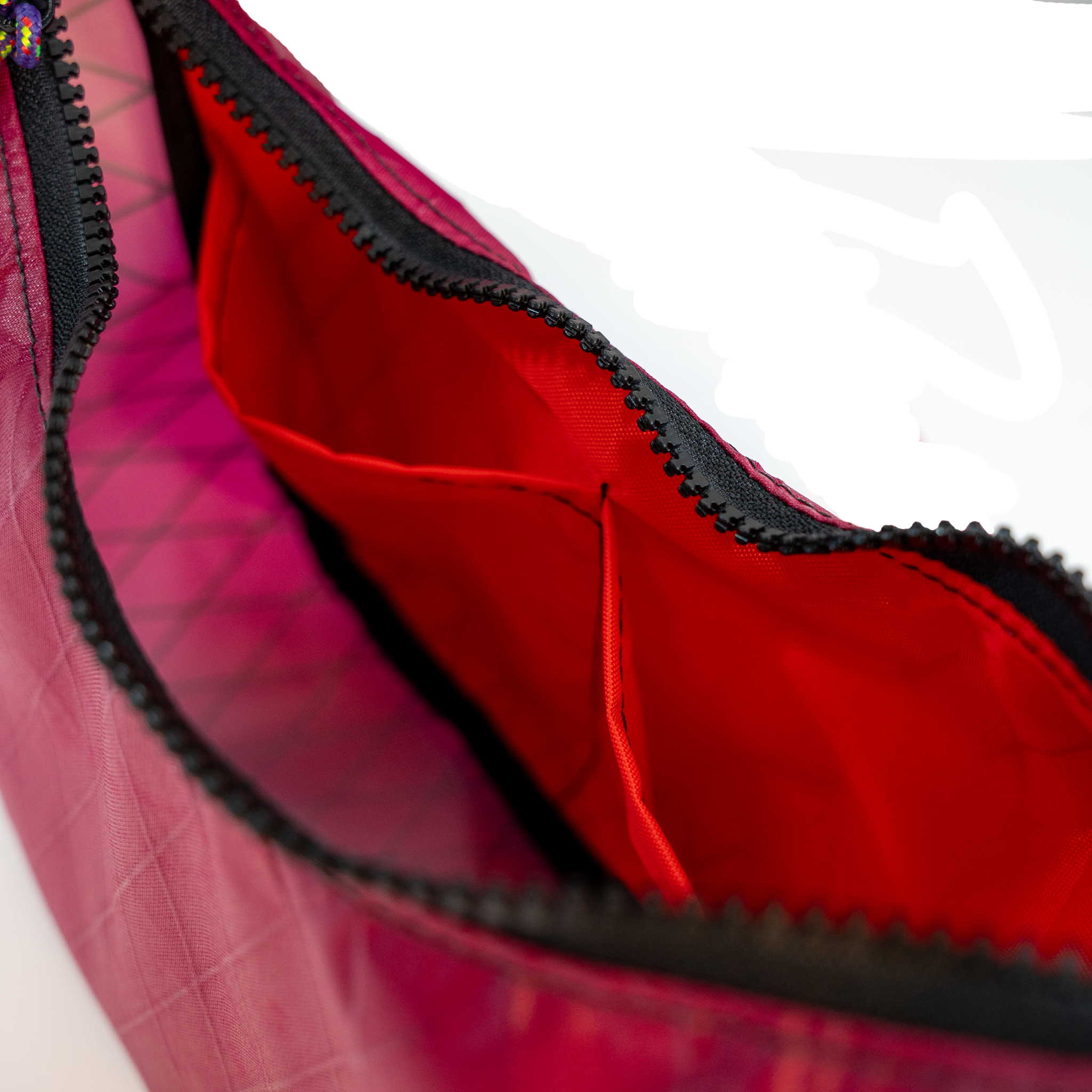 Close-up of a zippered bag showing a bright red interior lining and black zipper trim, with part of a magenta exterior visible.