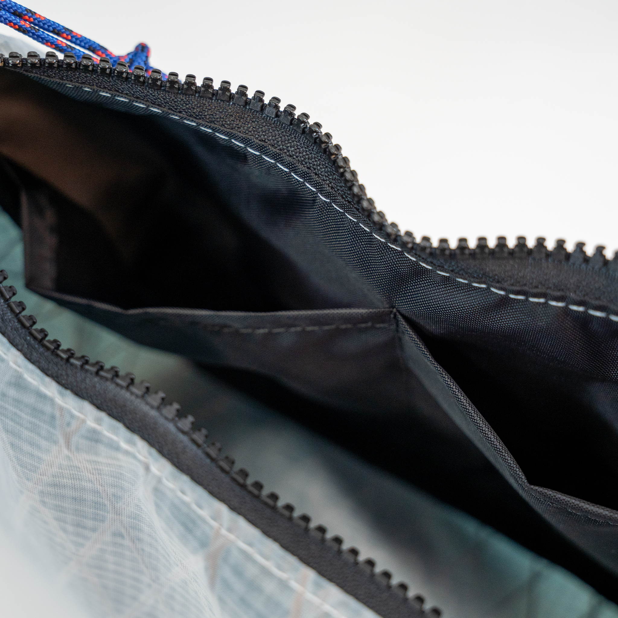 Close-up of a zippered bag showing the black interior lining, white stitching, and a white patterned exterior fabric with a black zipper trim.