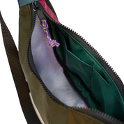 Close-up of an open bag showing the interior, with an olive green exterior, dark green lining, black zipper, and a purple-and-yellow knotted zipper pull on a white background.