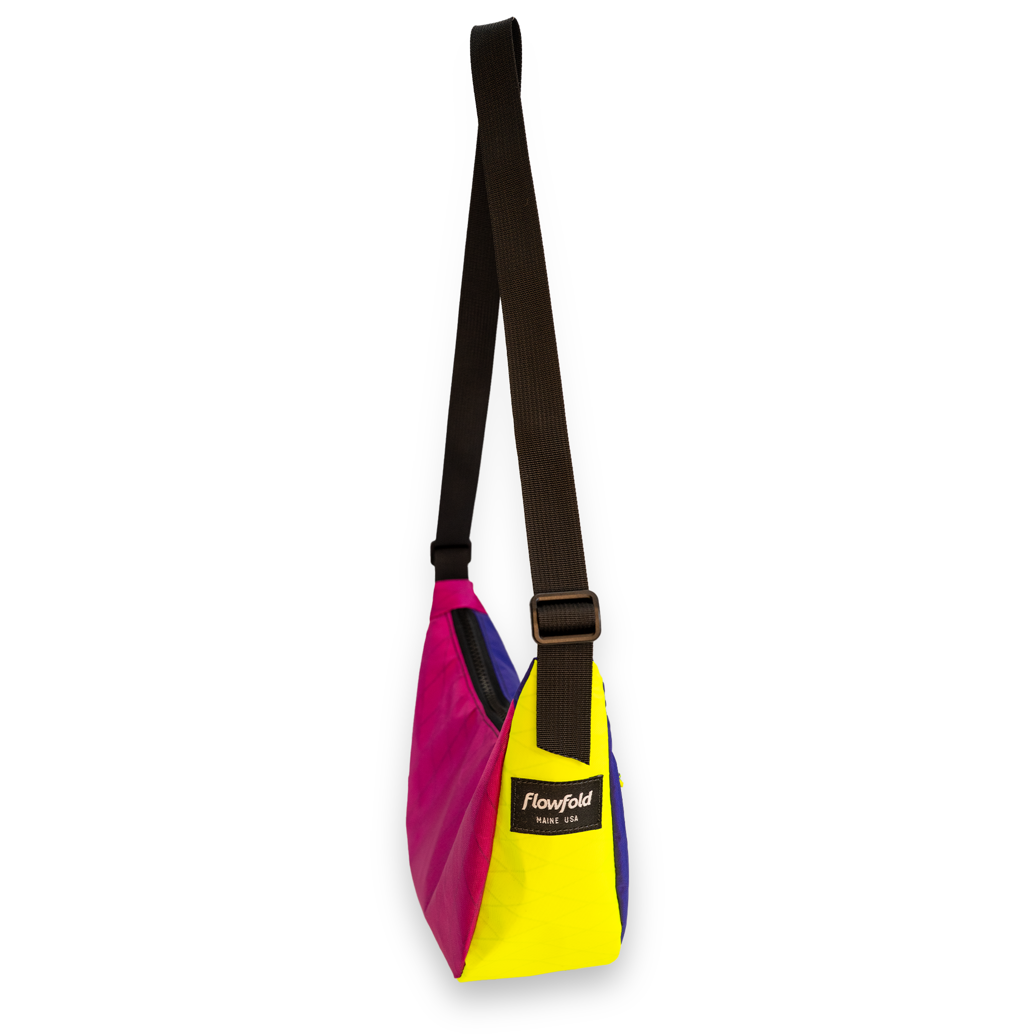 A Flowfold sling bag in a vibrant color-blocked design of magenta pink, yellow, and blue, featuring a wide black adjustable shoulder strap and a black brand label on the front.