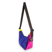 A color-blocked shoulder bag with a purple, pink, and yellow body, a black strap, and a black brand patch that reads 'Flowfold'.