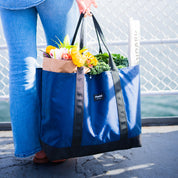 Person holding a blue reusable bag with groceries against a blurred background