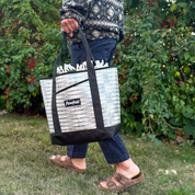 Person holding a black and white tote bag with 'Flowfold' branding outdoors.