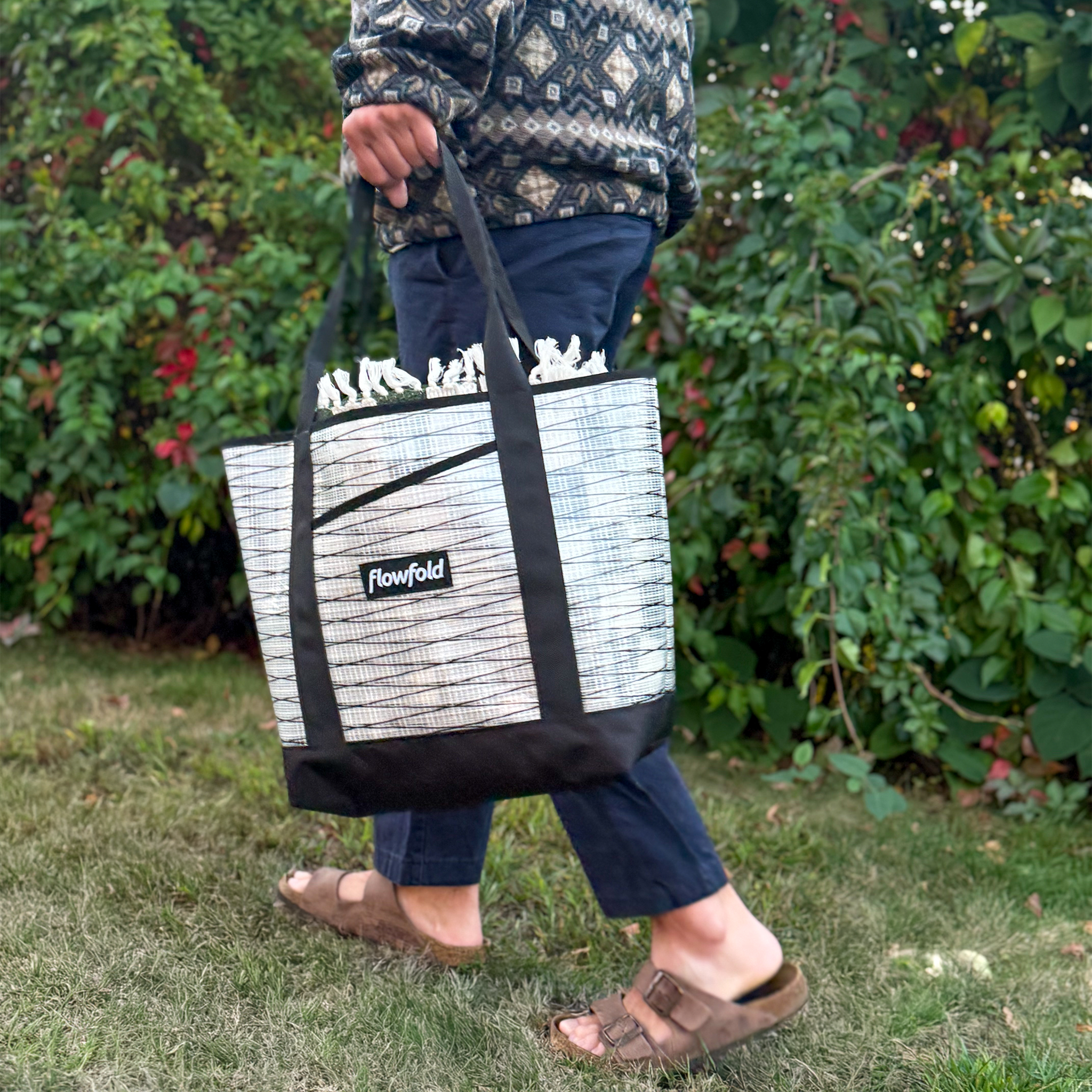 Person holding a black and white tote bag with 'Flowfold' branding outdoors.