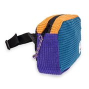 Side angle of a blue, orange, and purple fleece grid belt bag with black strap on a white background