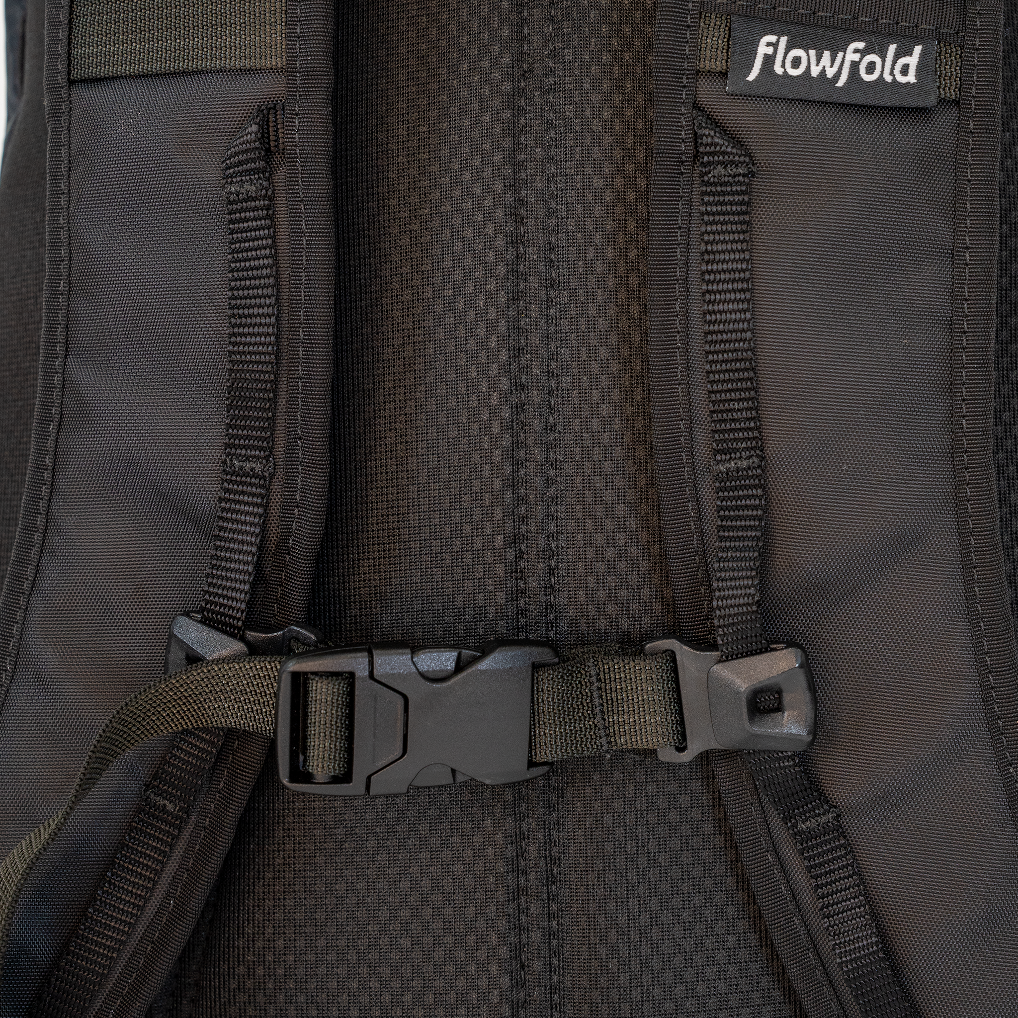 Close-up of a black Flowfold backpack showing the padded back panel, straps, and plastic buckle closure.