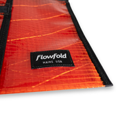 Close-up of a rust colored recycled sailcloth pouch with 'Flowfold' branding on a white background