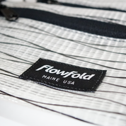 Close-up of a white recycled sailcloth pouch with 'Flowfold' branding on a white background